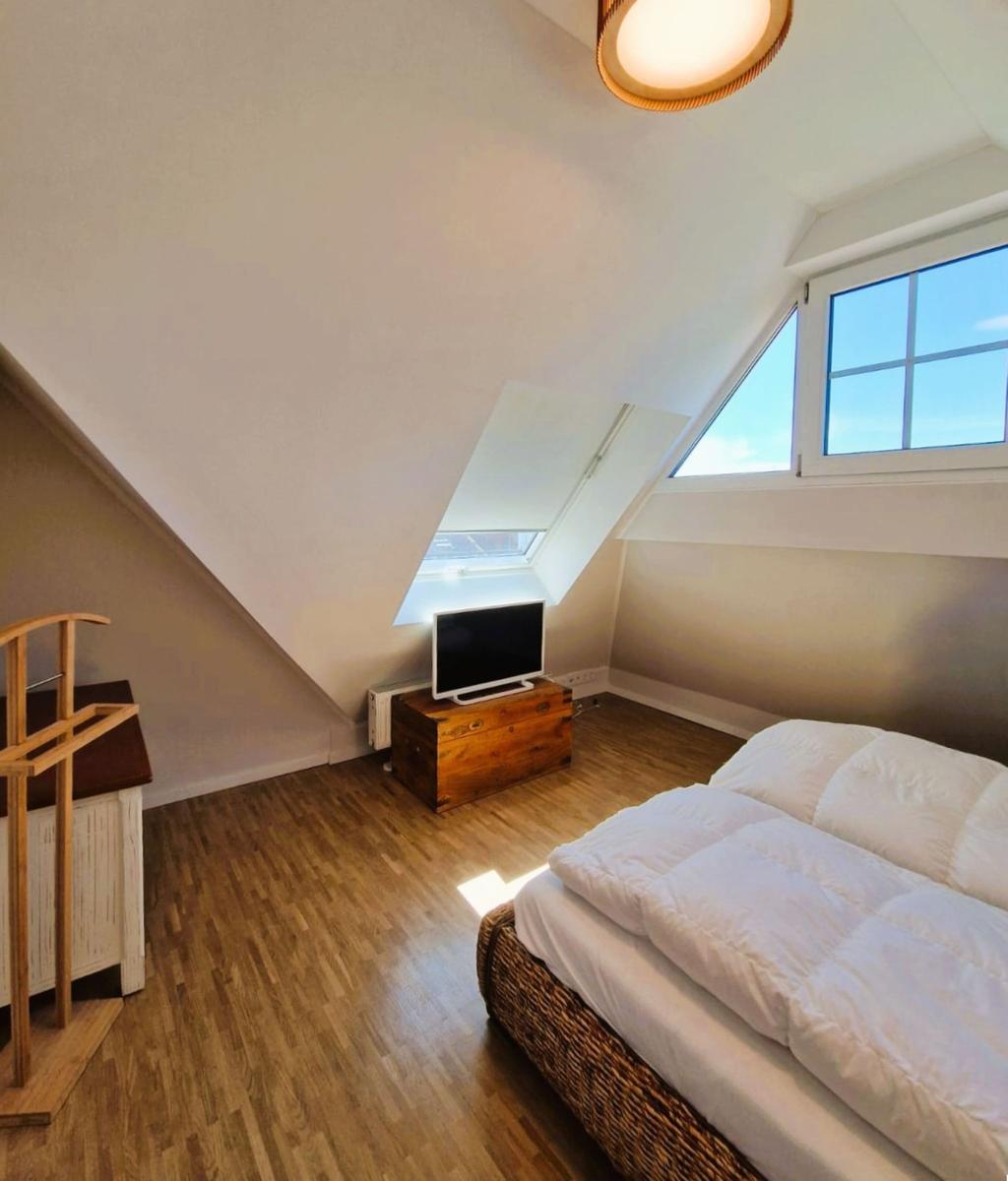 Schlafzimmer mit Dachschrägen, Fenster, TV und Holzboden.