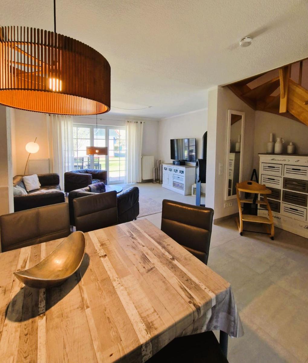 Essbereich mit Holztisch und Stühlen. Wohnbereich mit Sofa, Fernseher und Glasfront.
