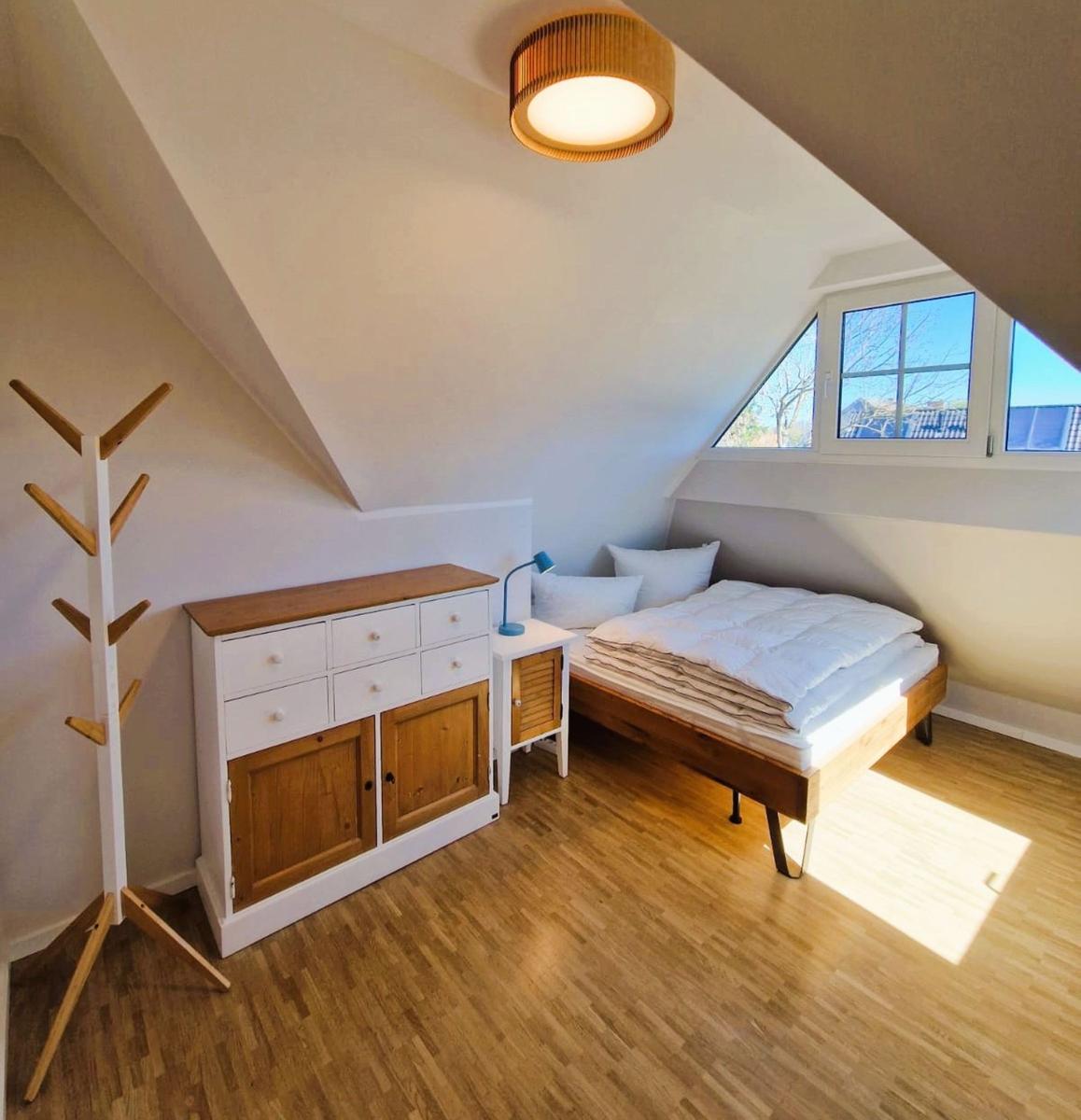 Schlafzimmer mit Dachschrägen, Holzboden, Bett, Schrank und Kleiderständer.