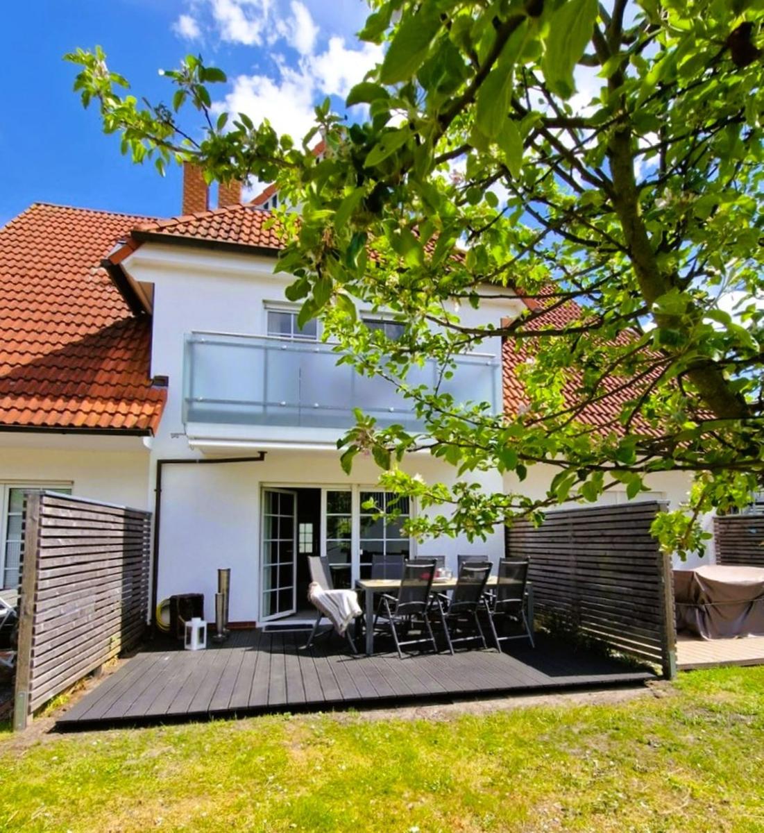 Haus mit Balkon, Terrasse und Garten. Holzgeländer und Tisch mit Stühlen.