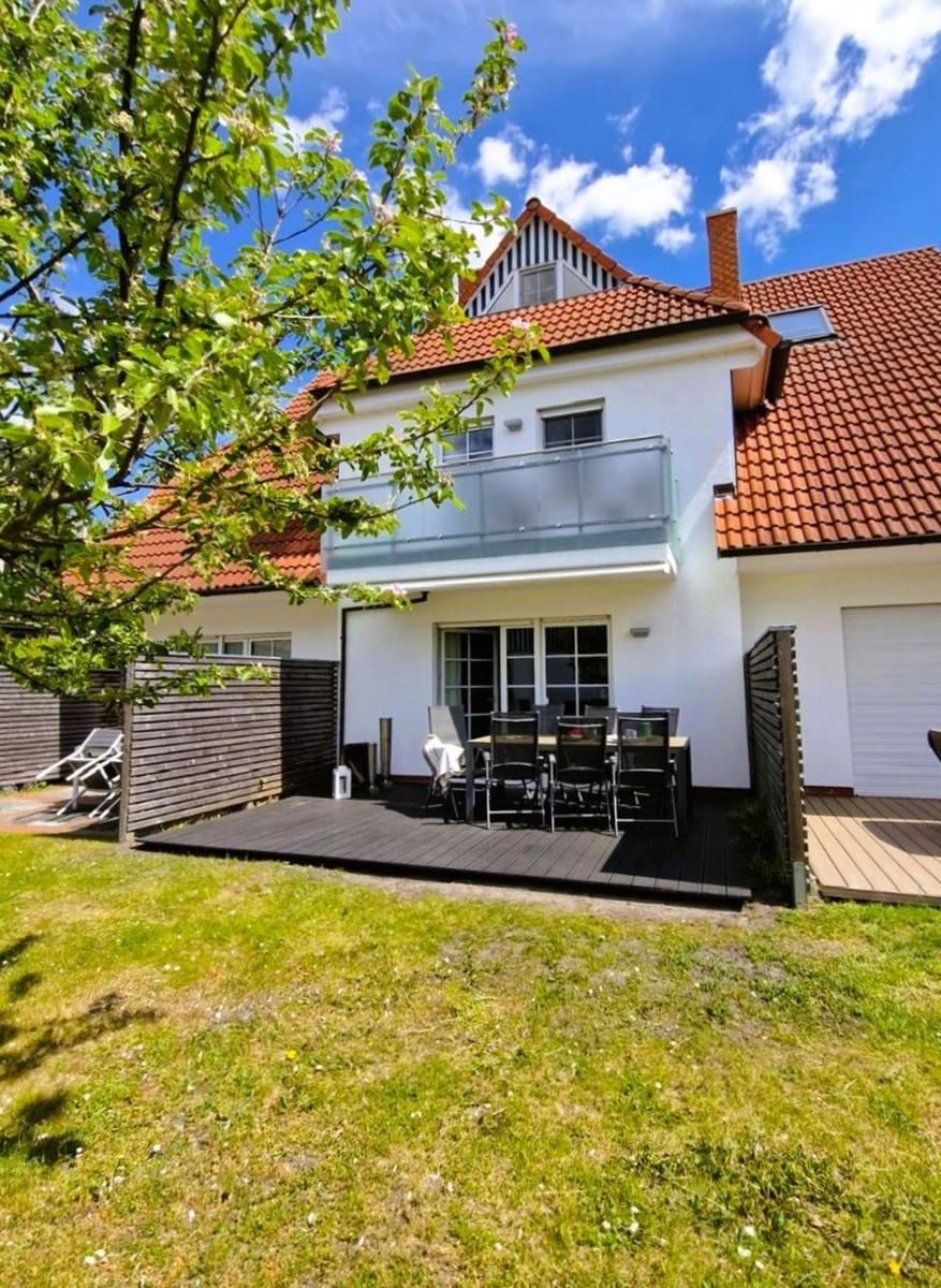 Haus mit Balkon, Terrasse und Garten unter blauem Himmel.