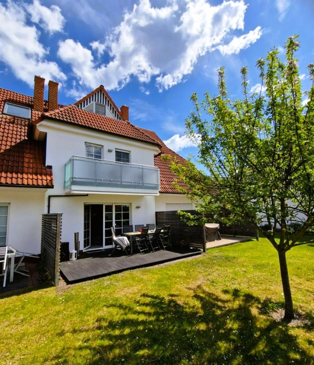 Wohnhaus mit Balkon, Terrasse und Garten unter blauem Himmel.