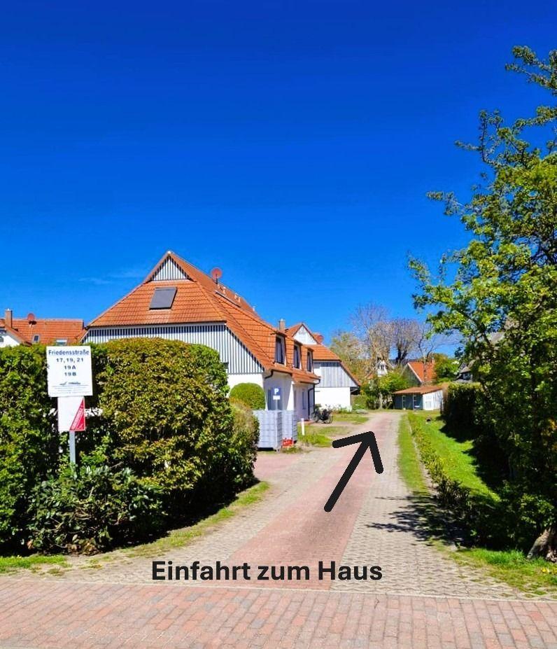 Pflasterweg führt zum Haus. Rote Dachziegel und grüne Bäume sind sichtbar.
