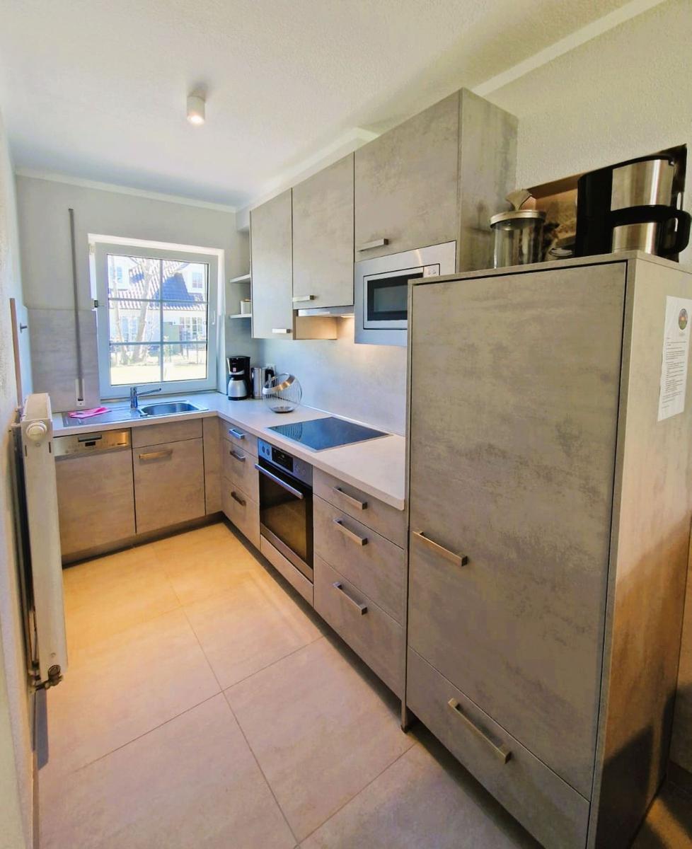 Küche mit Küchenschränken, Spüle, Herd und Kühlschrank. Fenster mit Blick nach draußen.