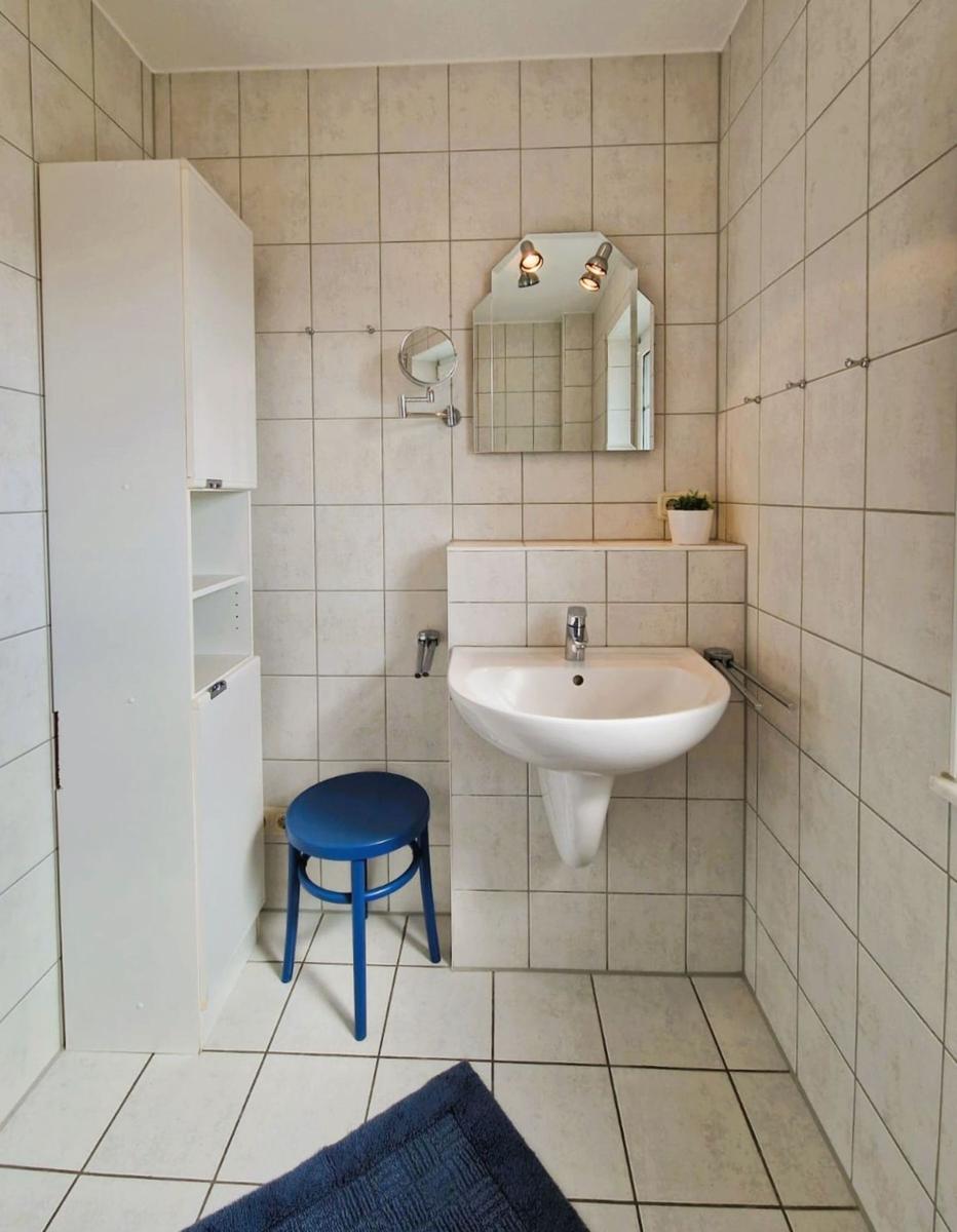 Badezimmer mit Waschbecken, Spiegel und blauem Hocker.
