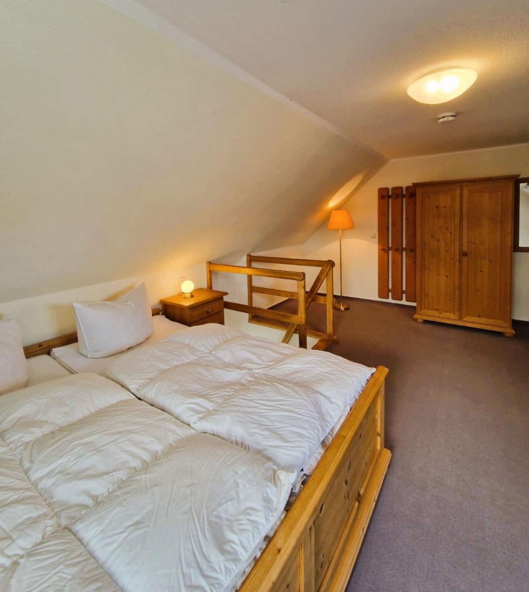 Schlafzimmer mit Doppelbett, Holzmöbel und schräger Decke.