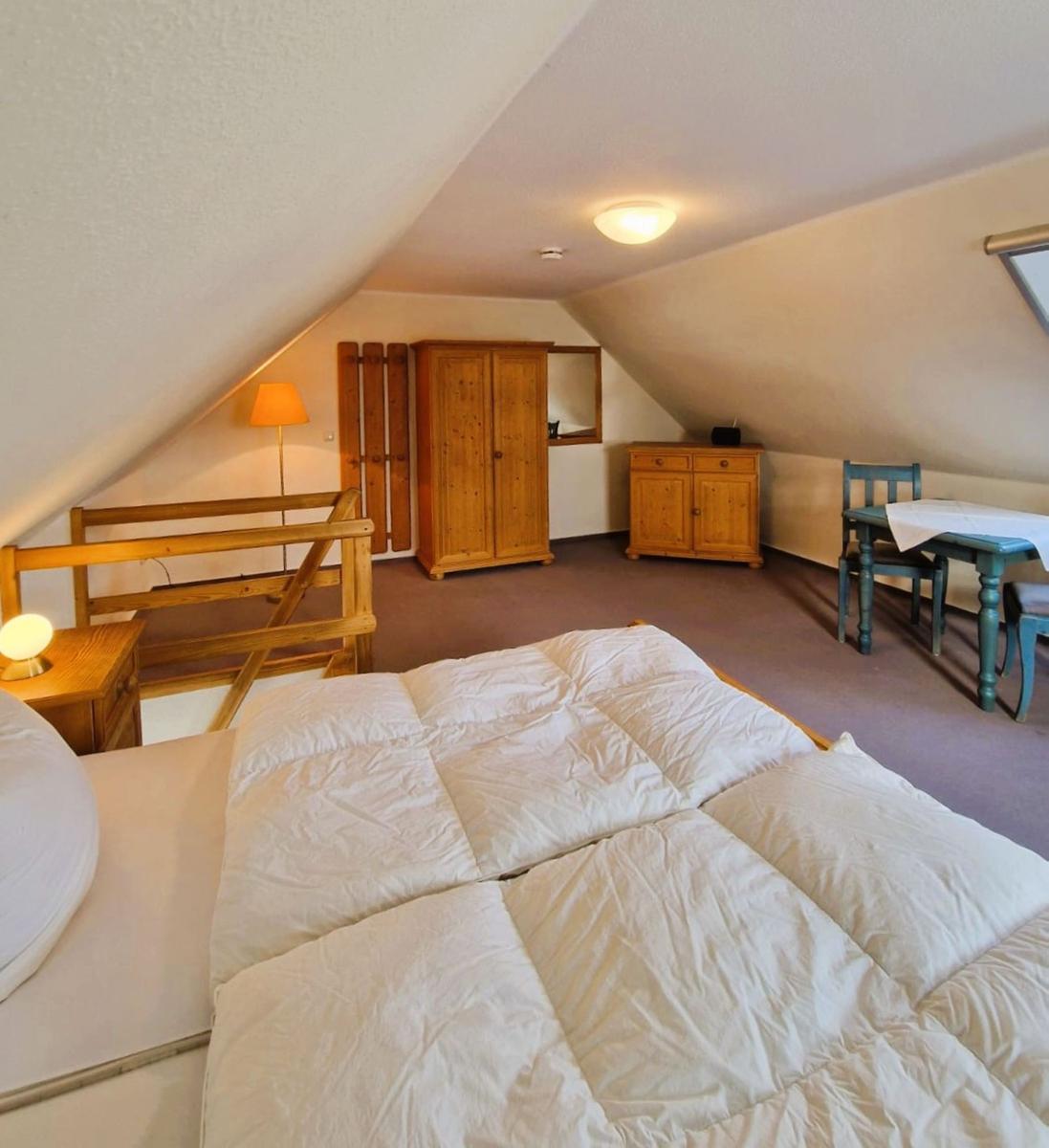 Schlafzimmer mit Dachschrägen, Bett, Schrank, Tisch und Stühle.