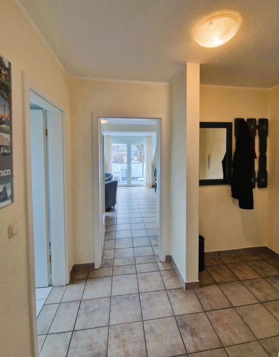 Flur mit Fliesenboden, Tür zu Wohnzimmer und Garderobe mit Spiegel und Mantelhaken.