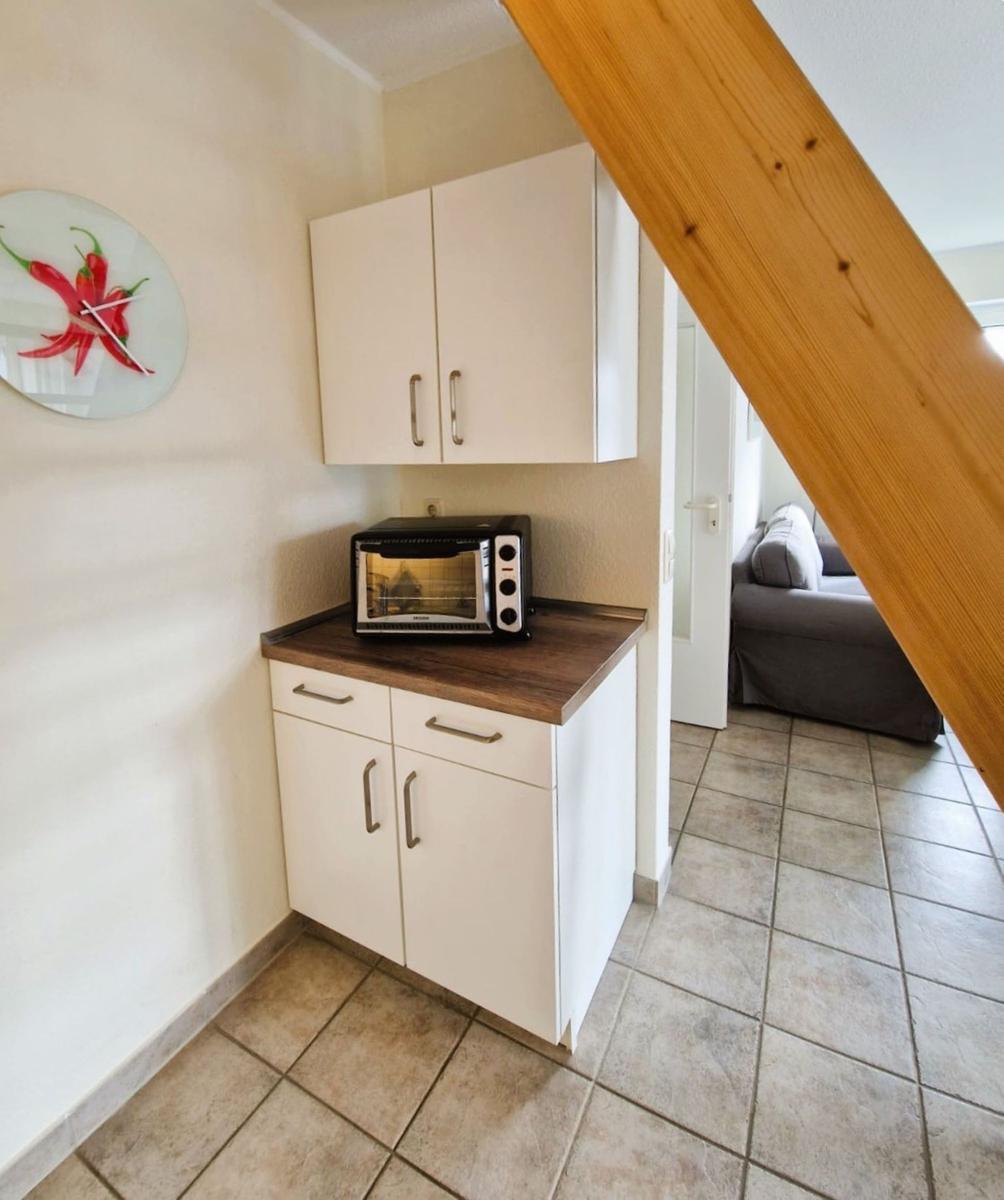 Küchenbereich mit weißen Schränken, Toaster und Wanduhr mit Paprika-Motiv.