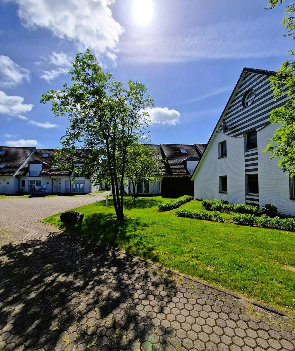 Haus mit grünem Rasen und gepflastertem Weg unter blauem Himmel.