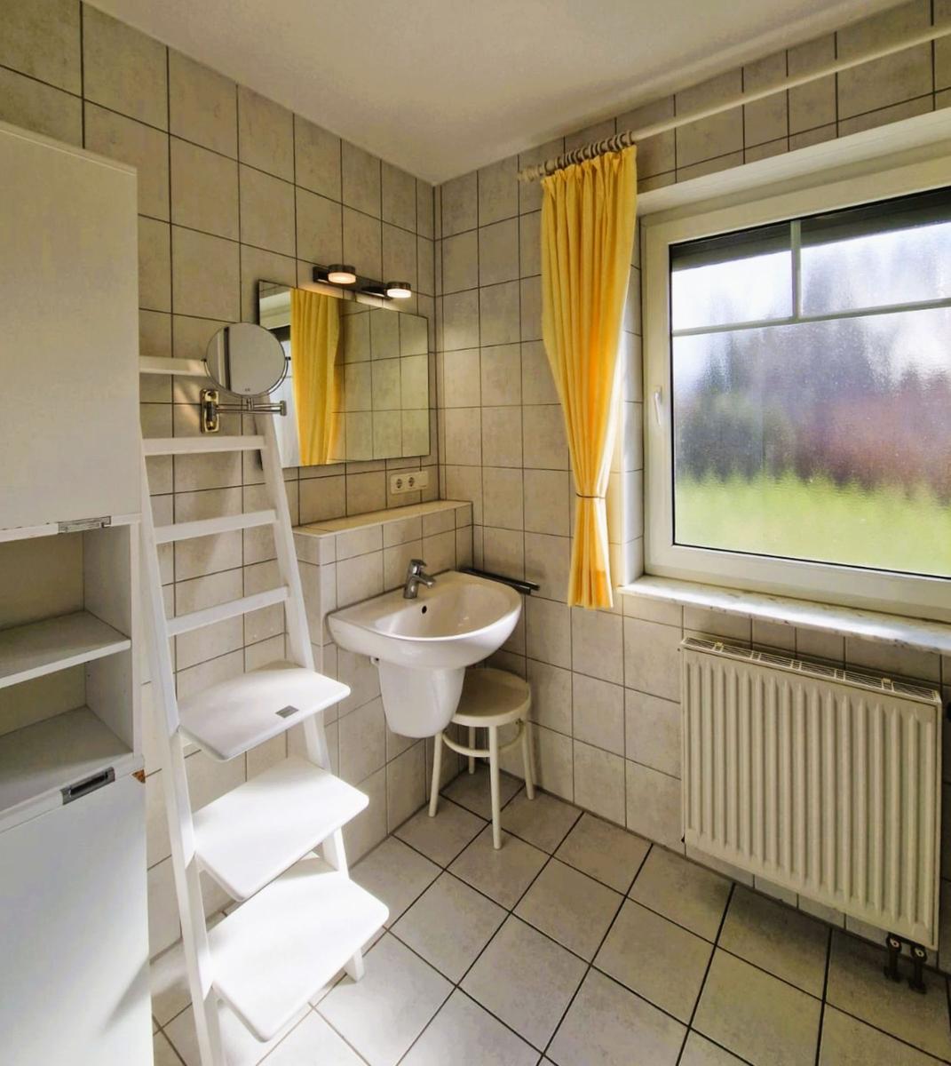 Badezimmer mit Waschbecken, Spiegel, Fenster und gelben Vorhängen.