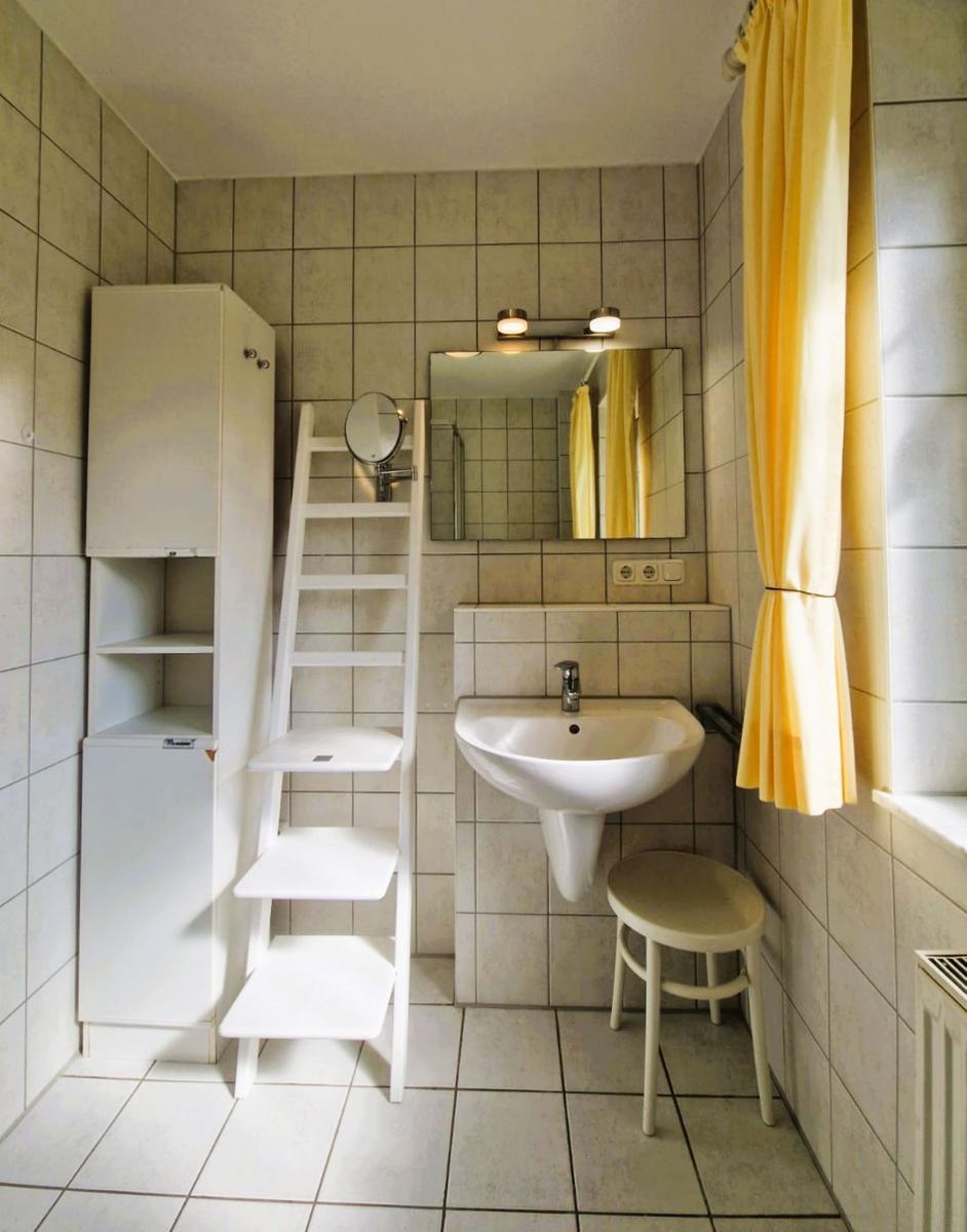 Badezimmer mit Waschbecken, Spiegel, Stuhl und Gardine.
