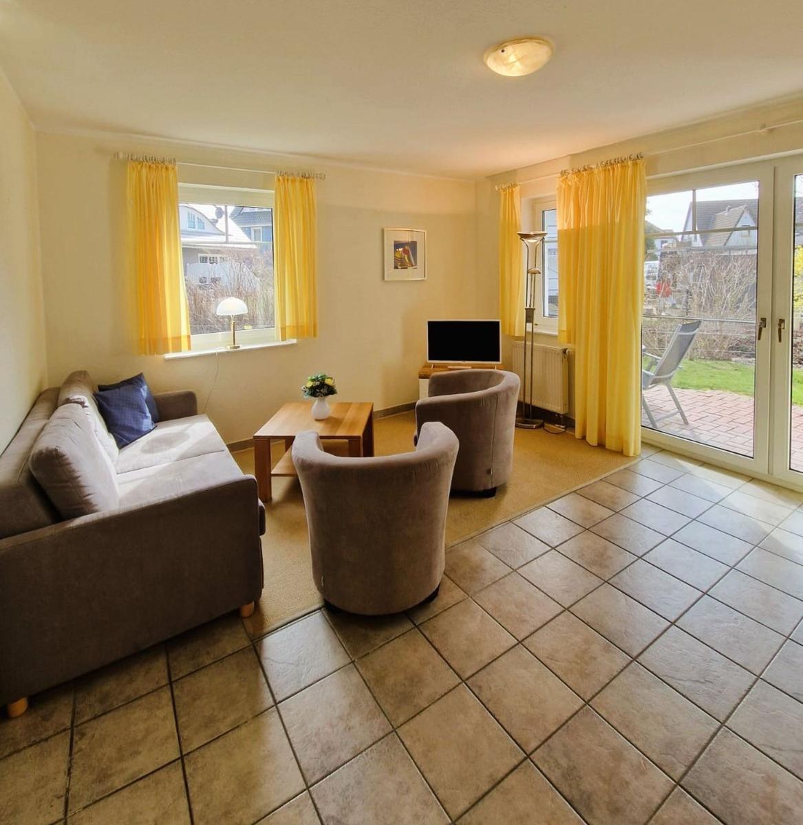 Wohnzimmer mit Sofa, zwei Sesseln, Fernseher und Terrasse mit Blick.