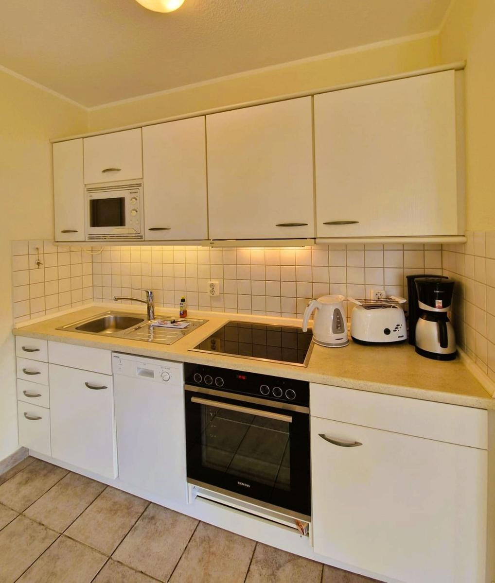 Küche mit weißen Schränken, Spüle, Herd und Backofen sowie Kaffeemaschine und Kaffeemaschine.