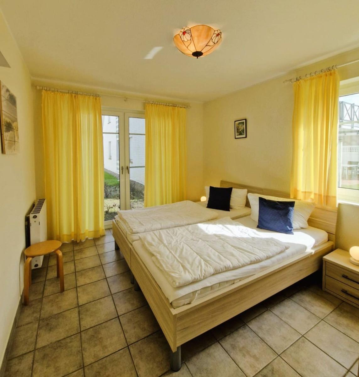 Schlafzimmer mit Doppelbett, gelben Vorhängen und Terrassentür.