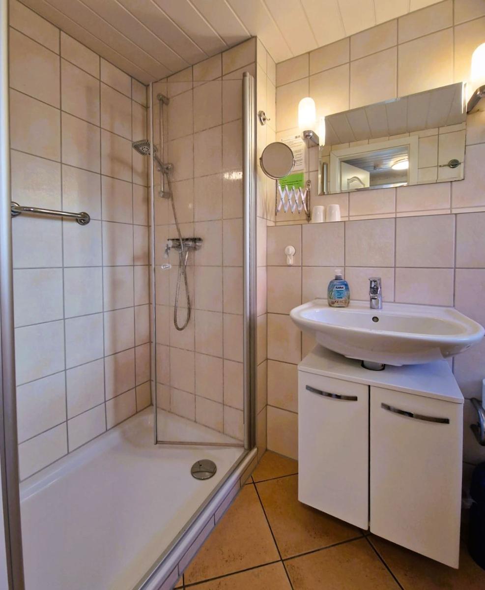 Shower cabin with shower head, sink, and mirror on the wall.