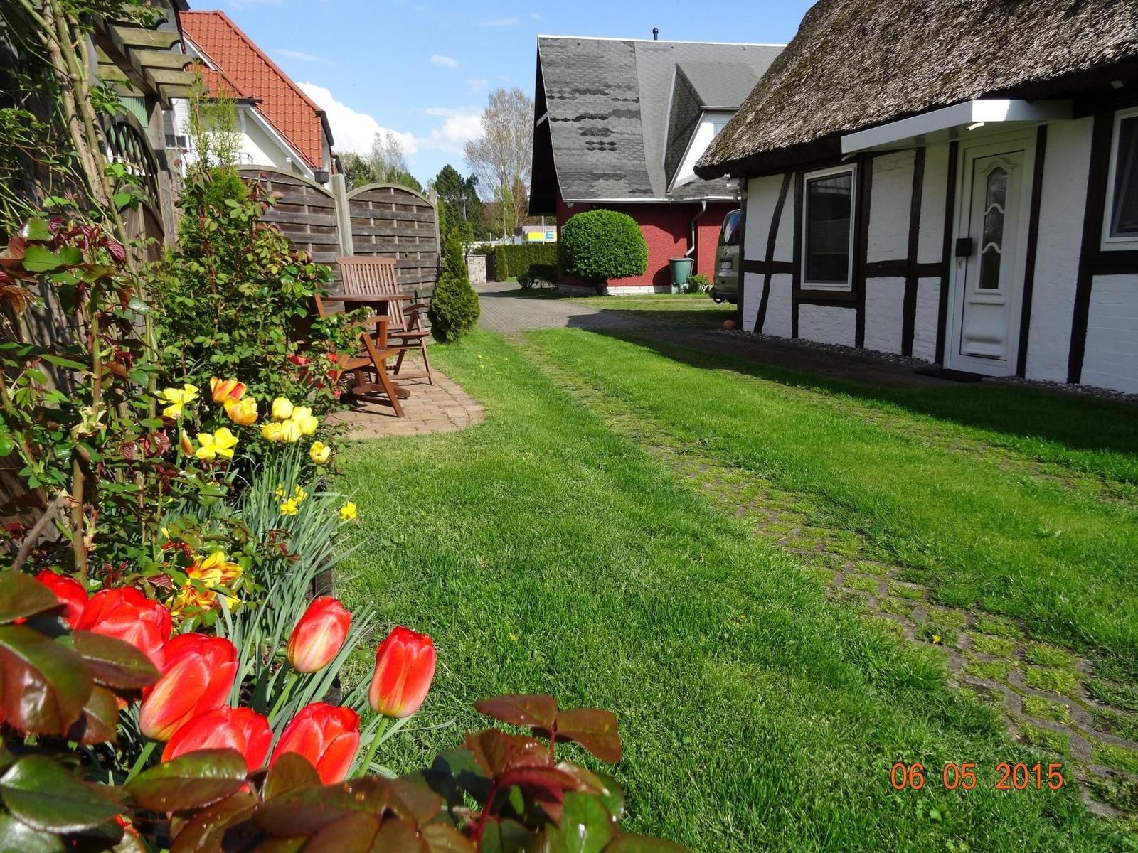 House with thatched roof, green lawn, and flower beds in the front garden.