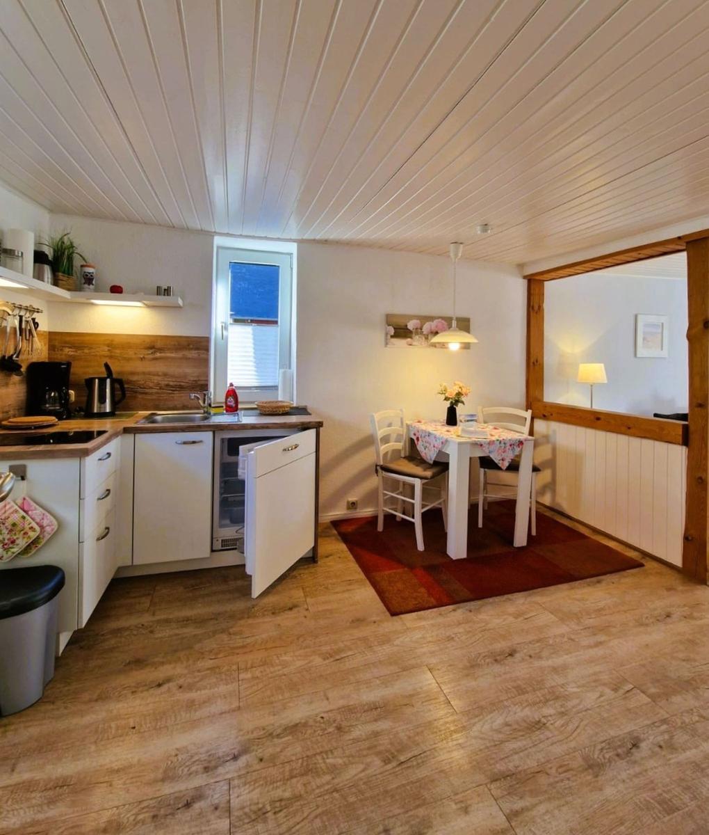 Kitchen with dining area, wooden floor, and white ceiling. Table with chairs and flowers.