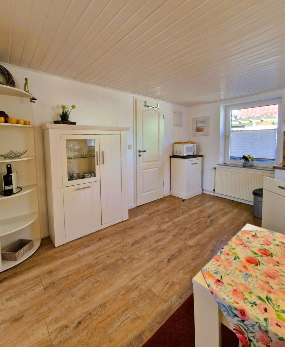 Kitchen with wooden floor, white cabinets, and window with view outside.