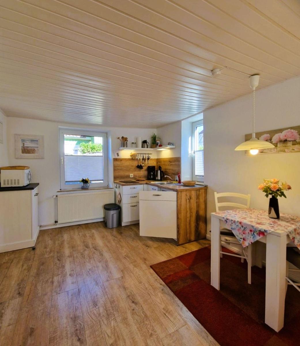 Kitchen with dining area, wooden floor, and windows. Table with tablecloth and flowers.
