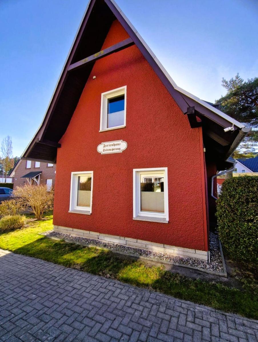 Red holiday house with white windows and sign. Front garden with lawn and gravel.