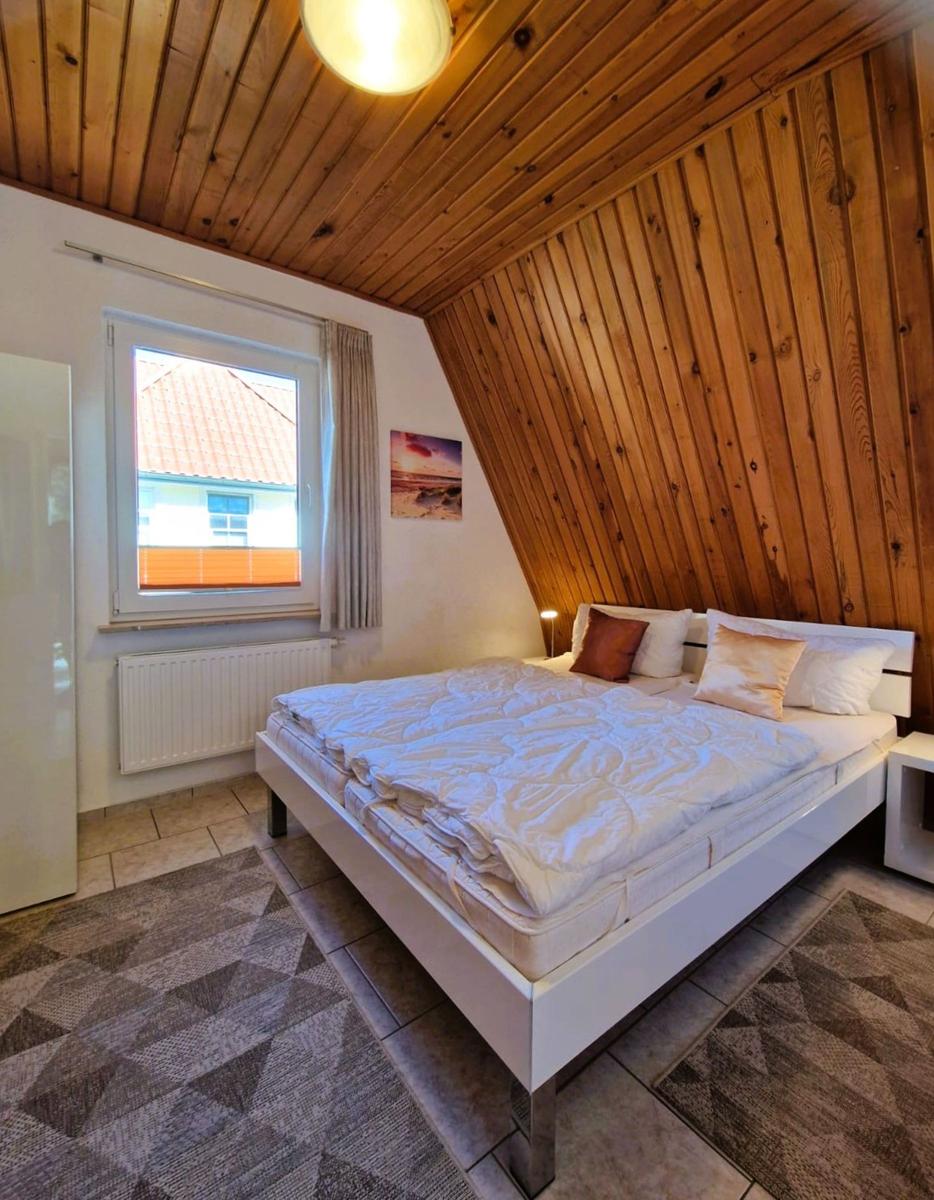 Bedroom with wooden wall, bed, and window with view of house