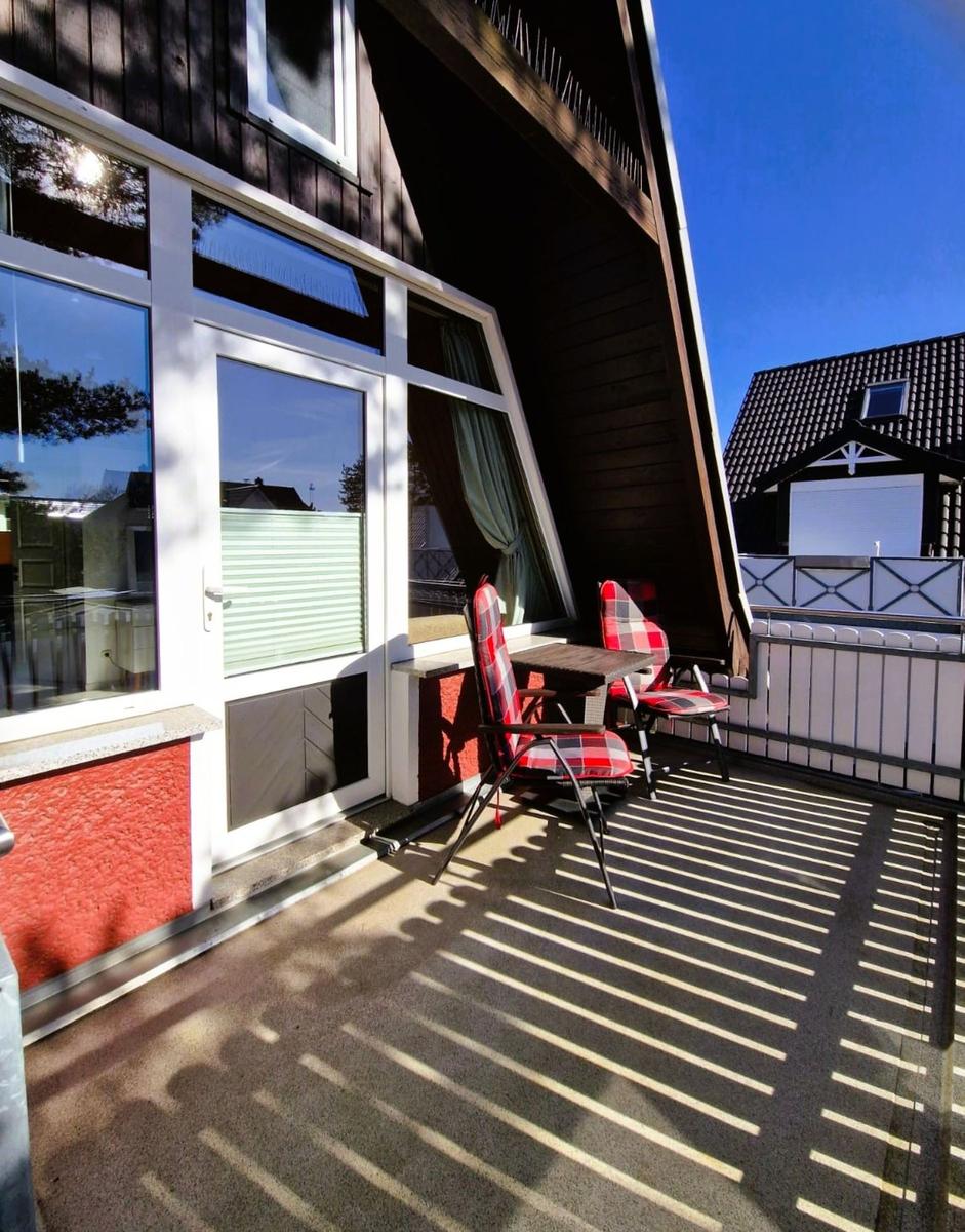 Terrace with table and two chairs in front of a house with large windows.