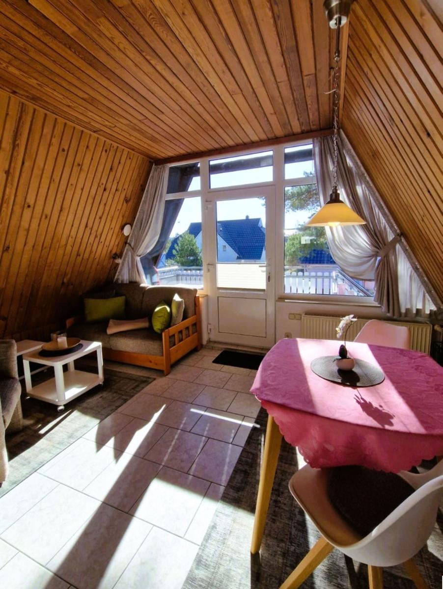 Living area with wooden ceiling, sofa, dining table with tablecloth, and window to balcony.