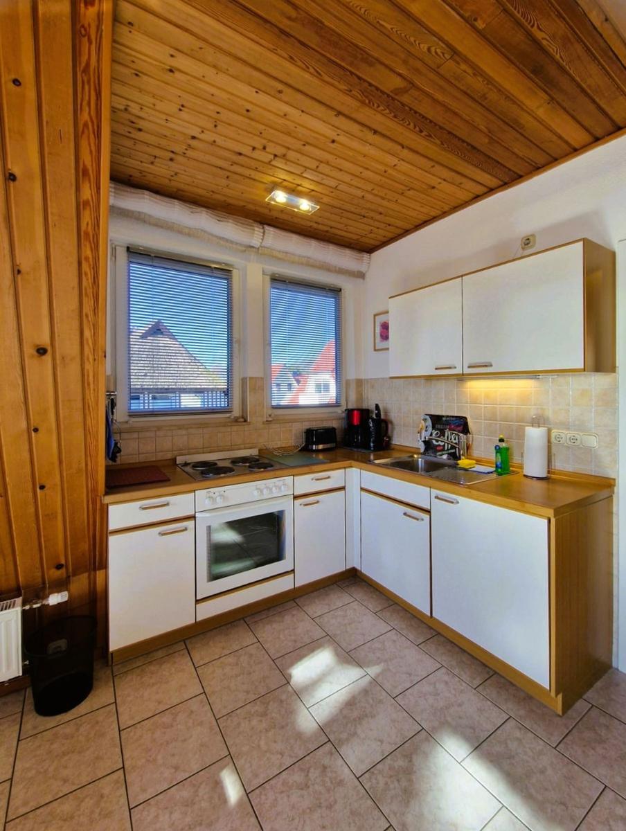 Kitchen with wooden ceiling, white cabinets, and windows with blinds.