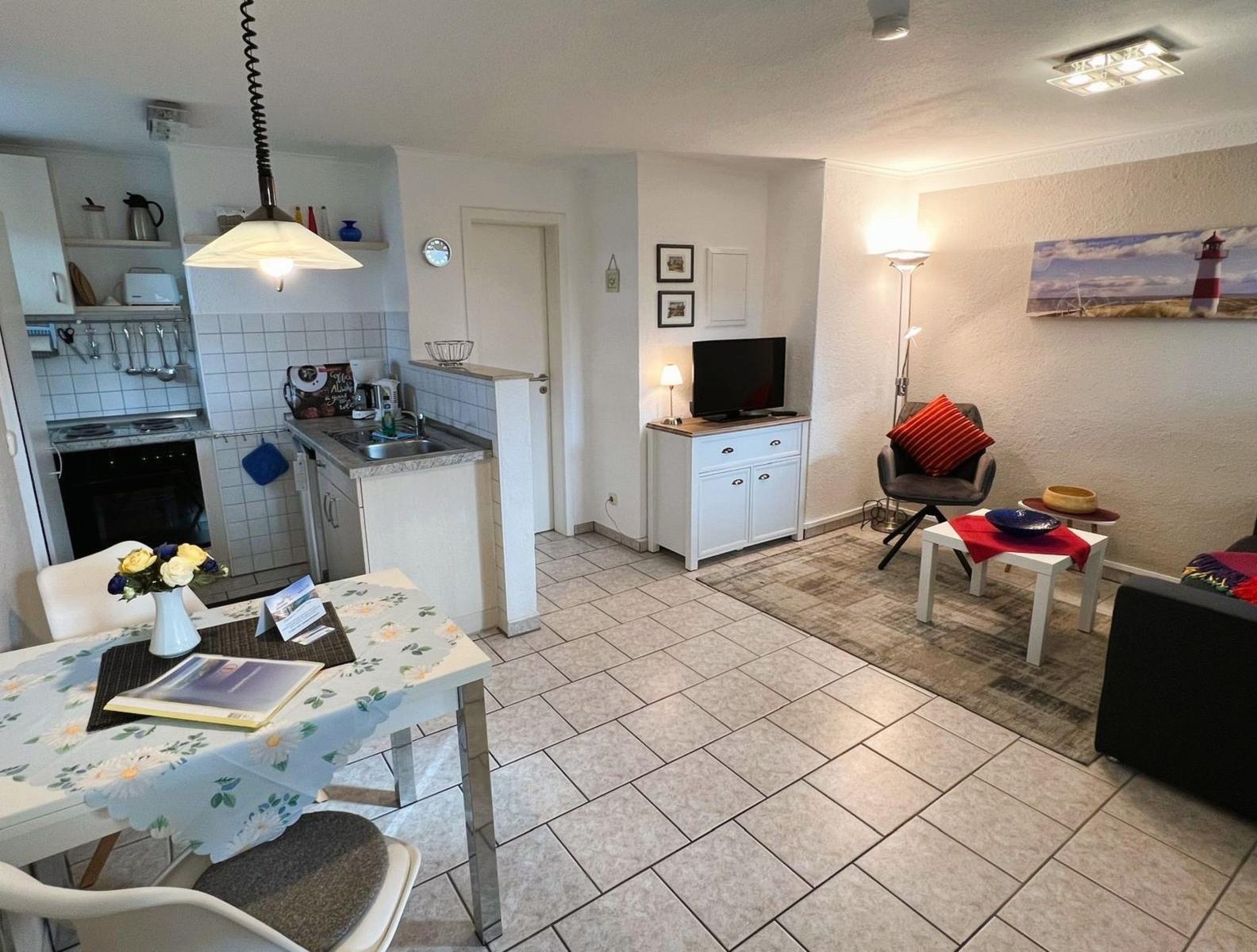 Living kitchen with dining area, TV, and seating. Tile floor and wall art with lighthouse.