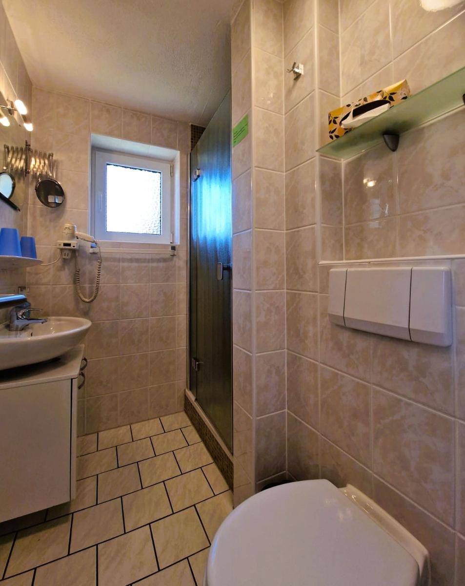 Bathroom with shower, sink, and toilet. Tiled walls and window visible.