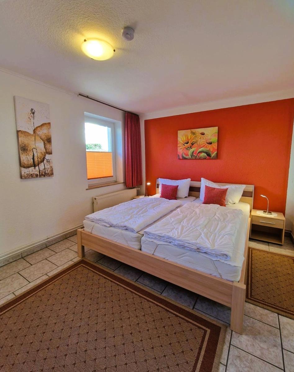 Bedroom with double bed, orange wall, and window with blinds.