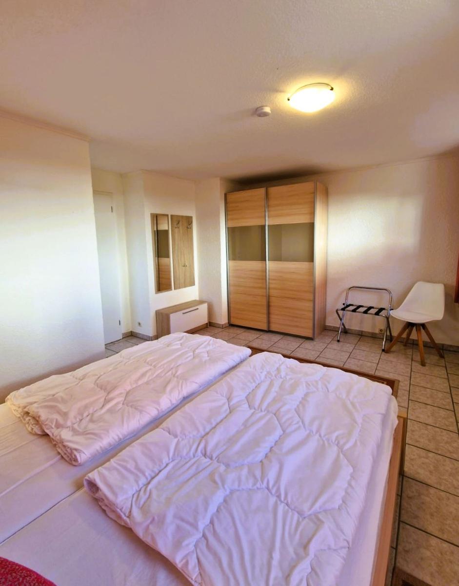 Room with double bed, wardrobe, and chair on tiled floor.
