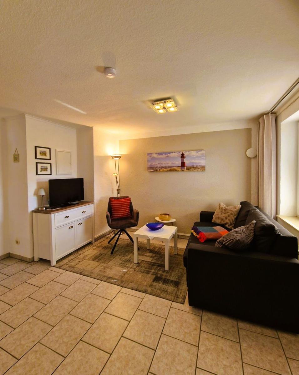 Living room with sofa, armchair, TV, and wall art with lighthouse