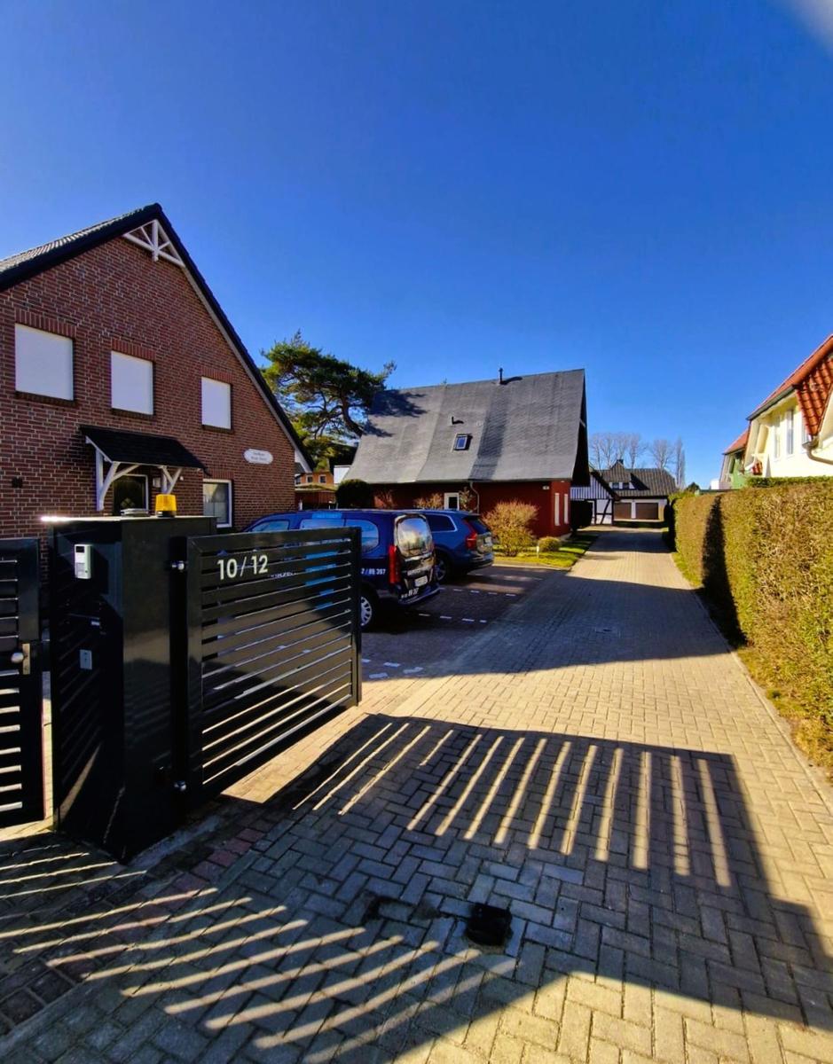 Gate marked 10/12, paved path, parked cars in front of houses.