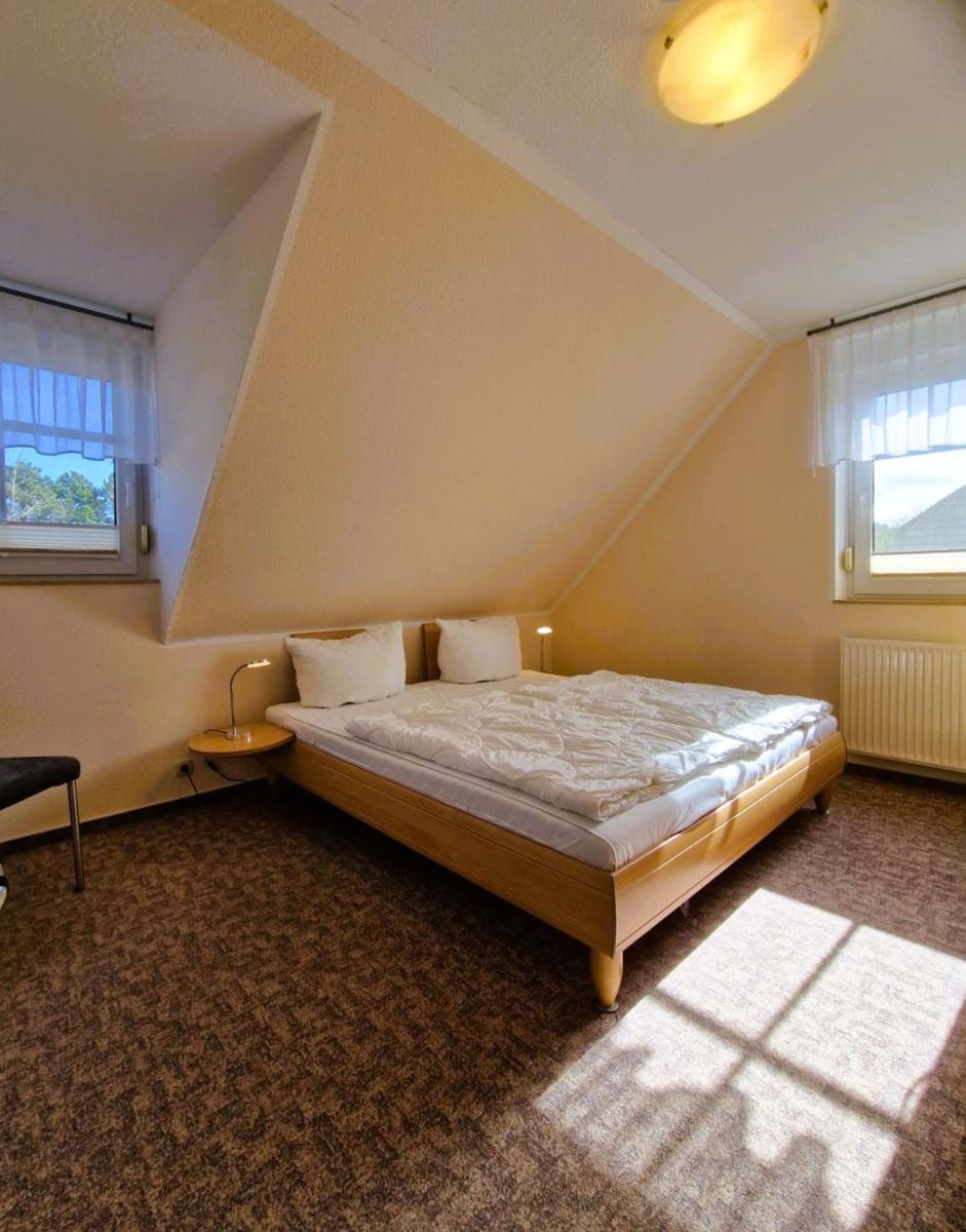 Schlafzimmer mit Dachschräge, Bett, zwei Fenster und Teppichboden.