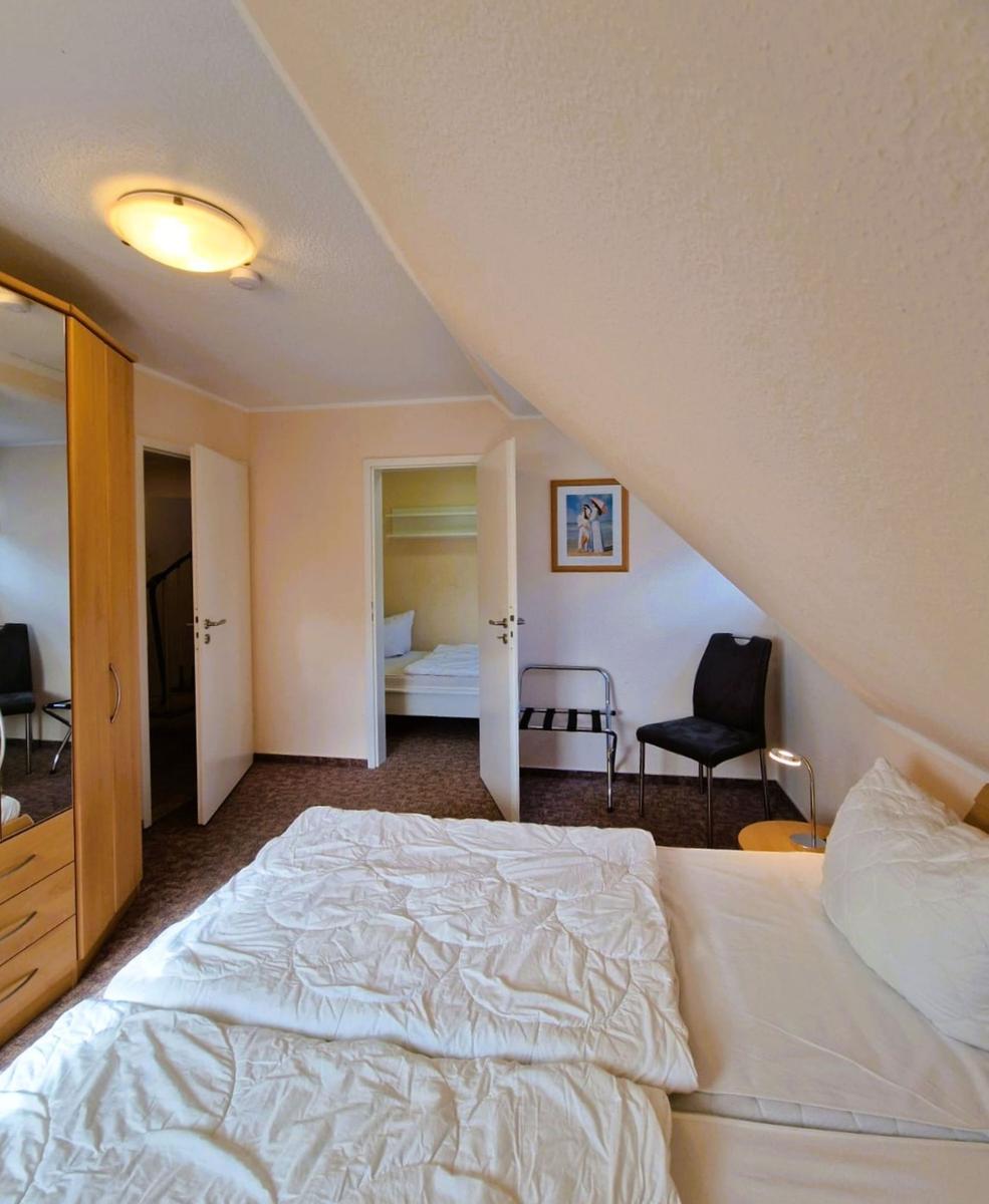 Schlafzimmer mit Dachschrägen, Bett, Stuhl und Kleiderschrank. Tür führt in Schlafzimmer.