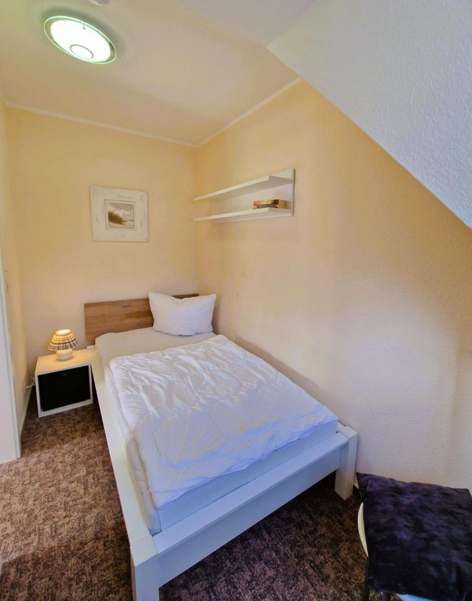 Schlafzimmer mit Bett, Nachttisch, Wandregal und Deckenleuchte.
