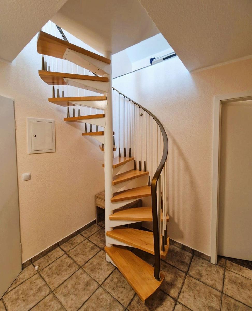Spiralförmige Treppe mit Holzstufen und Metallgeländer führt nach oben.