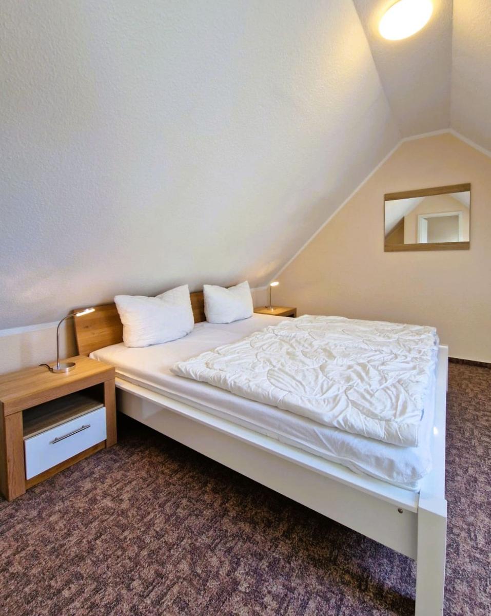 Schlafzimmer mit Doppelbett, Nachttischen und Spiegel an geneigter Wand.