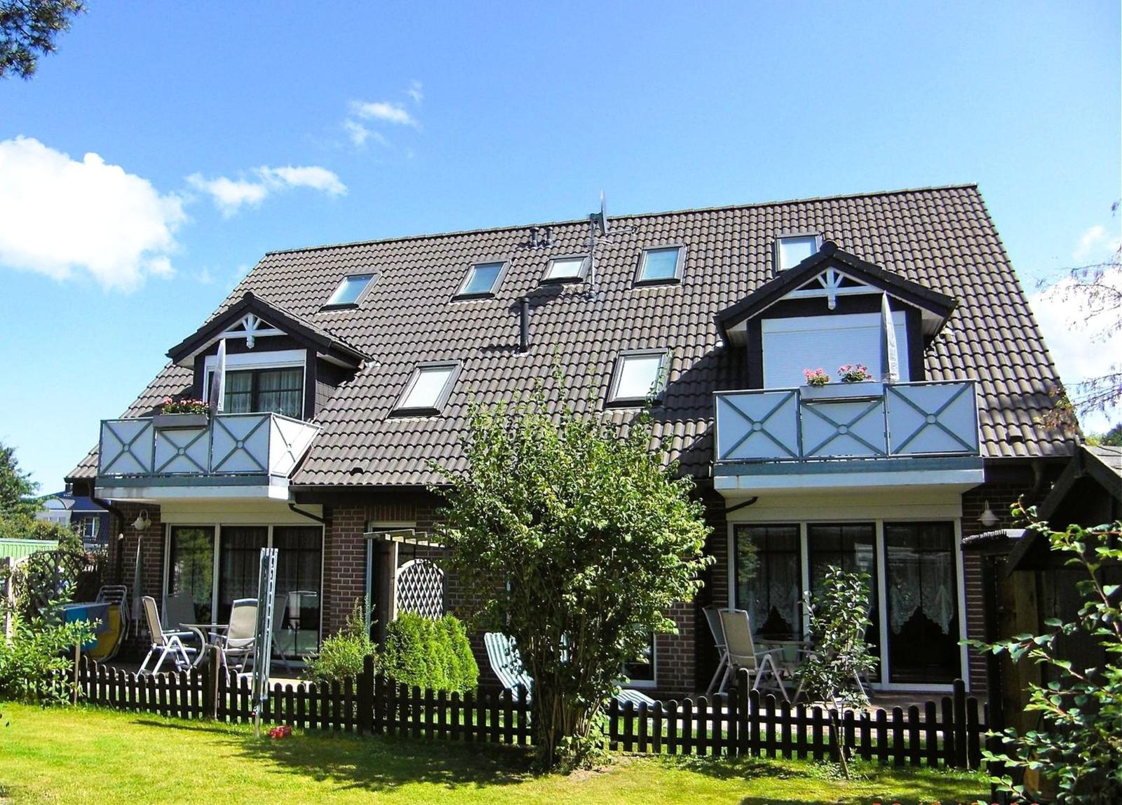 Ein zweistöckiges Haus mit Balkonen und Dachfenstern. Vorgarten mit Zaun und Gartenmöbeln.
