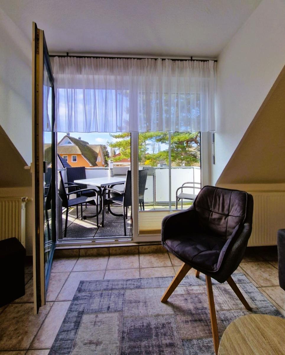 Ein Raum mit einem Stuhl und Blick auf eine Terrasse mit Tisch und Stühlen.