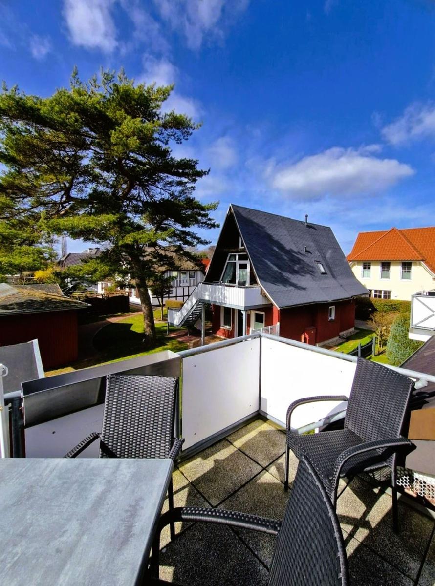 Terrasse mit Tisch und Stühlen. Blick auf rotes Haus und Baum unter blauem Himmel.