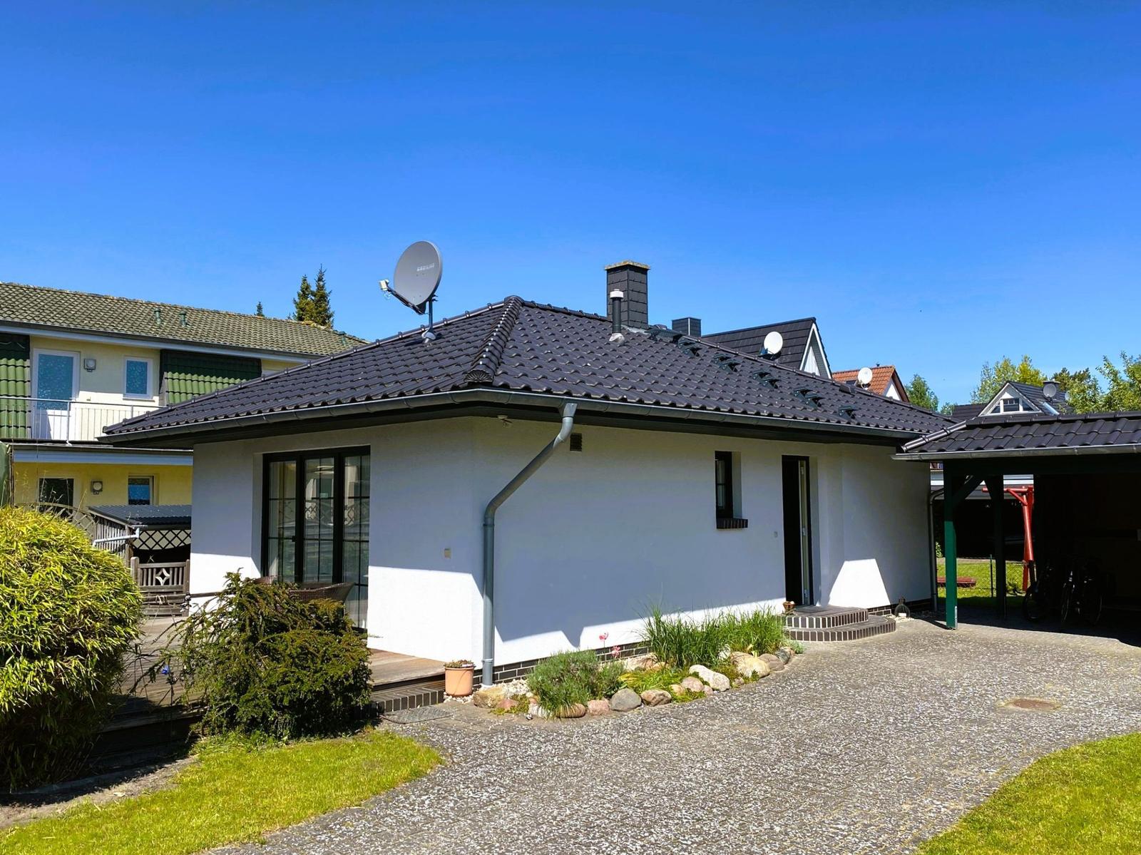 A white house with a dark roof, satellite dish, and gravel driveway.