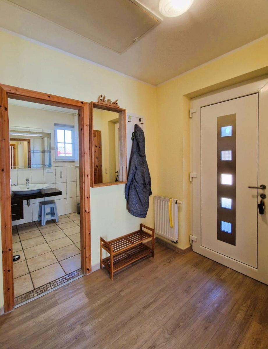 Entrance with wooden floor, mirror, and door with glass panels. View into the bathroom.