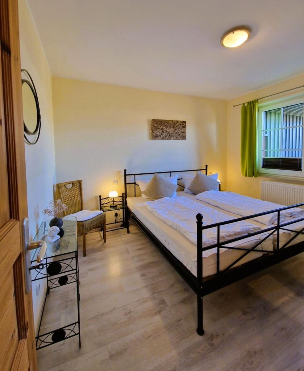 Bedroom with double bed, nightstand, chair, and window with green curtains.