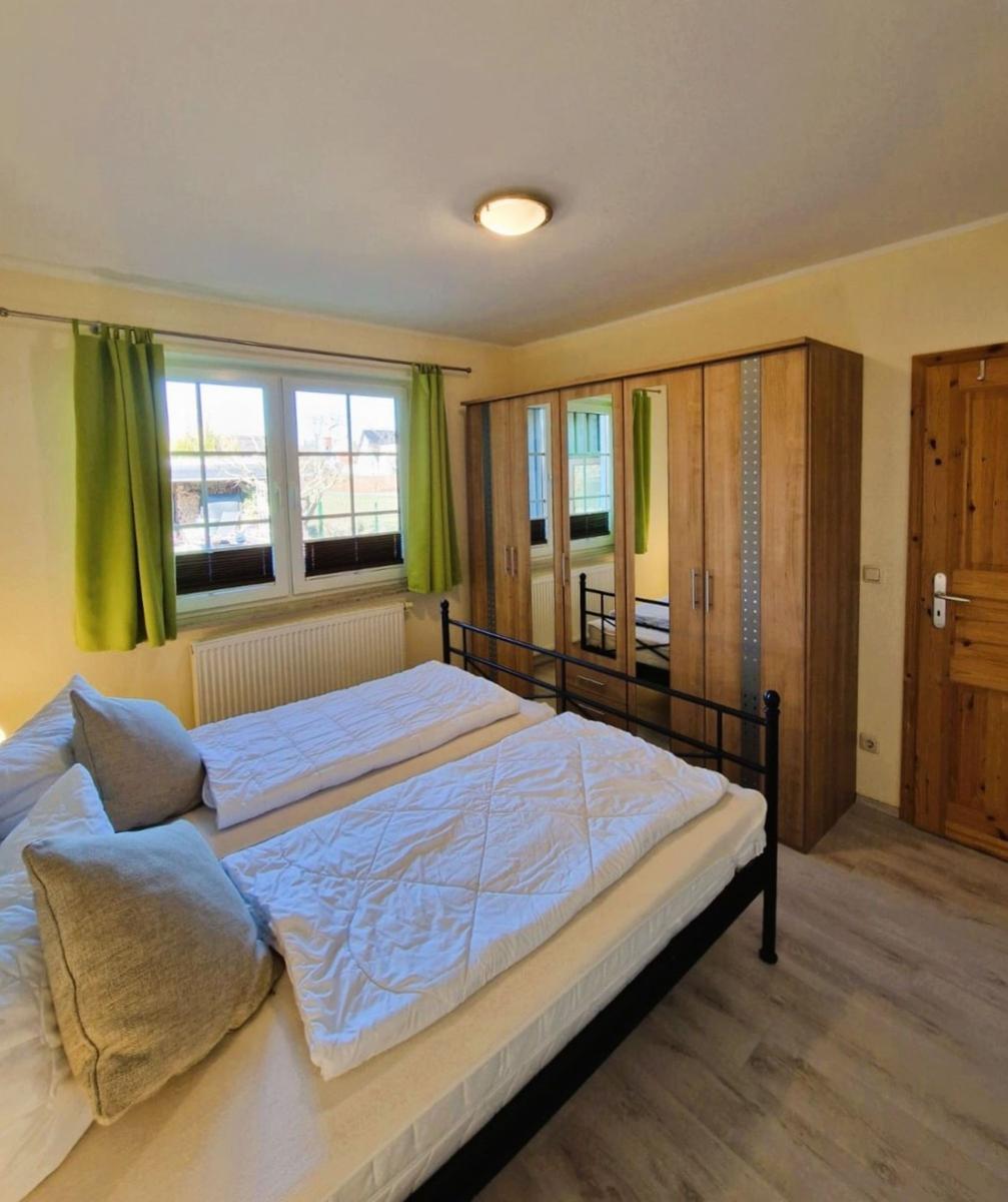 Bedroom with double bed, wooden wardrobe, and window with green curtains.