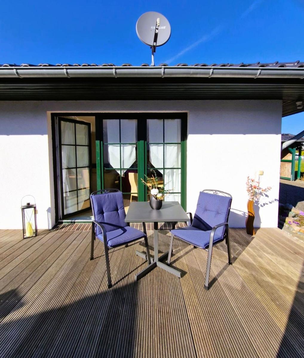 Terrace with table and two chairs, view into living area with green window frames.