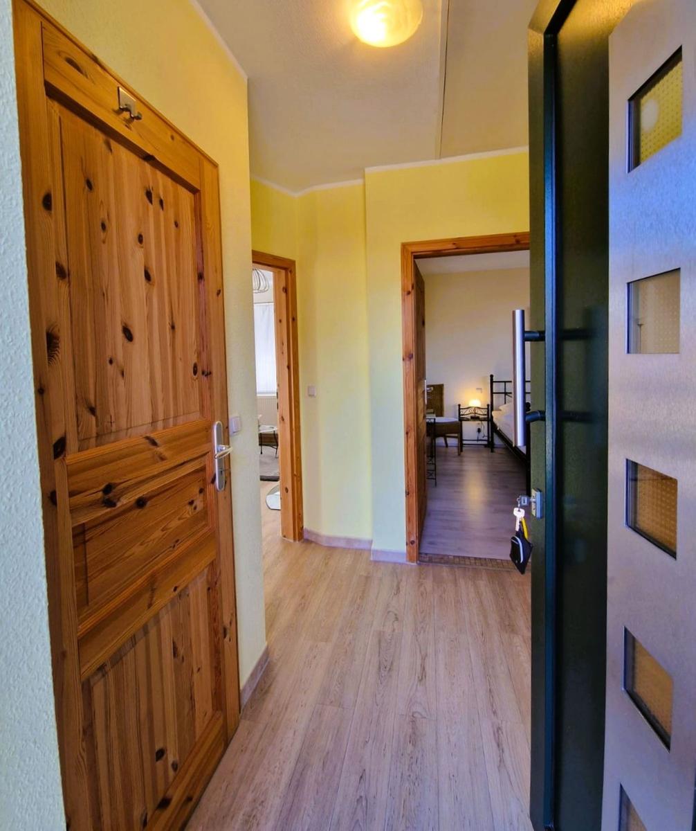 Hallway with wooden doors and light. View into bedroom with bed and table.