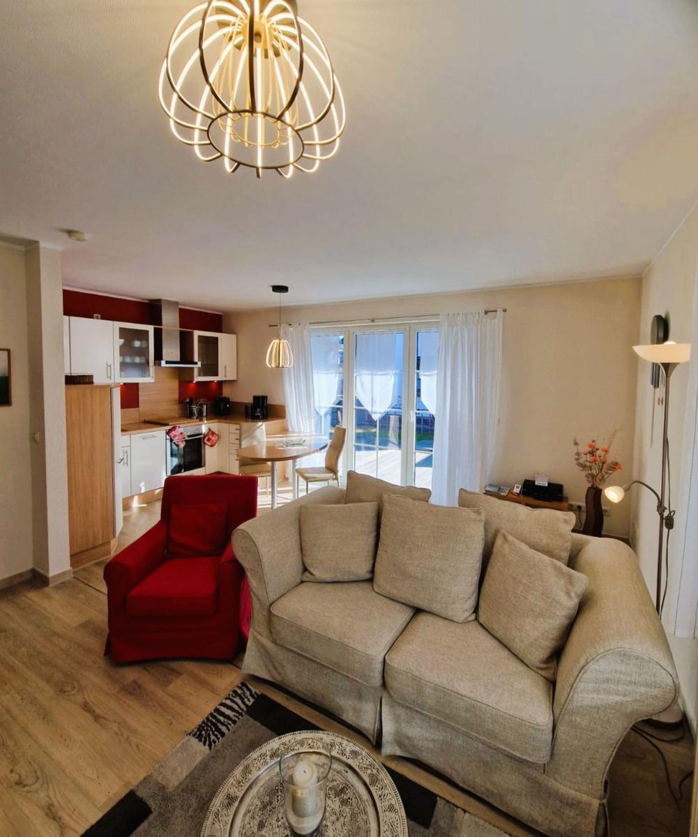Living area with sofa, red armchair, and kitchen area in the background.